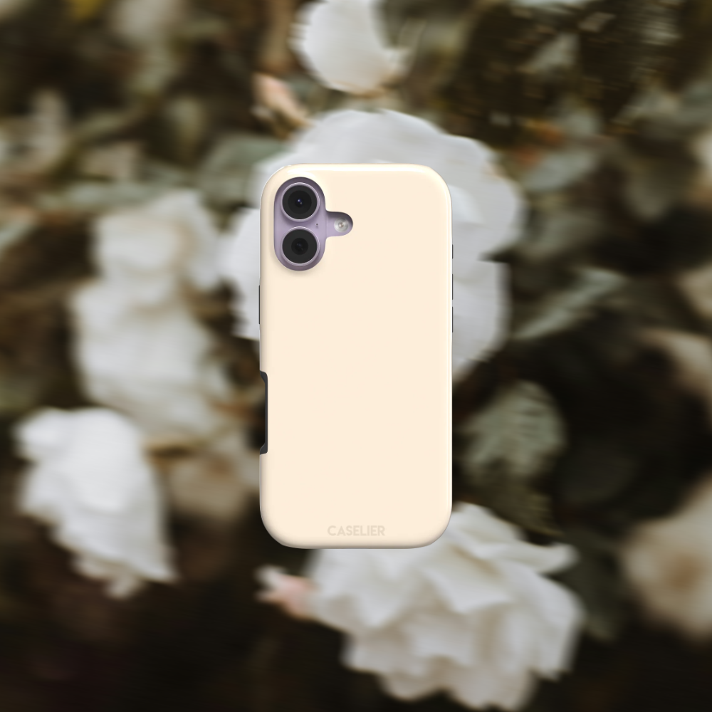 A cream-colored protective phone case with a dual-camera cutout, featuring the caselier written at the bottom, set against a blurred background of white flowers and green foliage.
