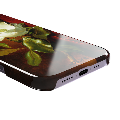 A Magnolia on Red Velvet by Martin Johnson Heade phone case showing a luminous white magnolia bloom with deep green leaves against rich red velvet drapery on a warm amber background, phone case by Caselier — snap case, charging port detail
