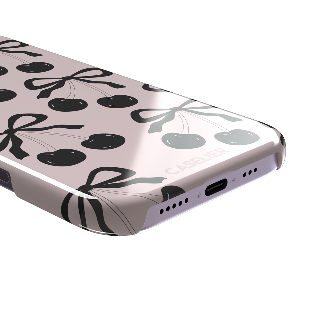Black Cherry phone case with an all-over pattern of black cherries and ribbon bows on a blush pink background, phone case by Caselier — snap case, charging port detail