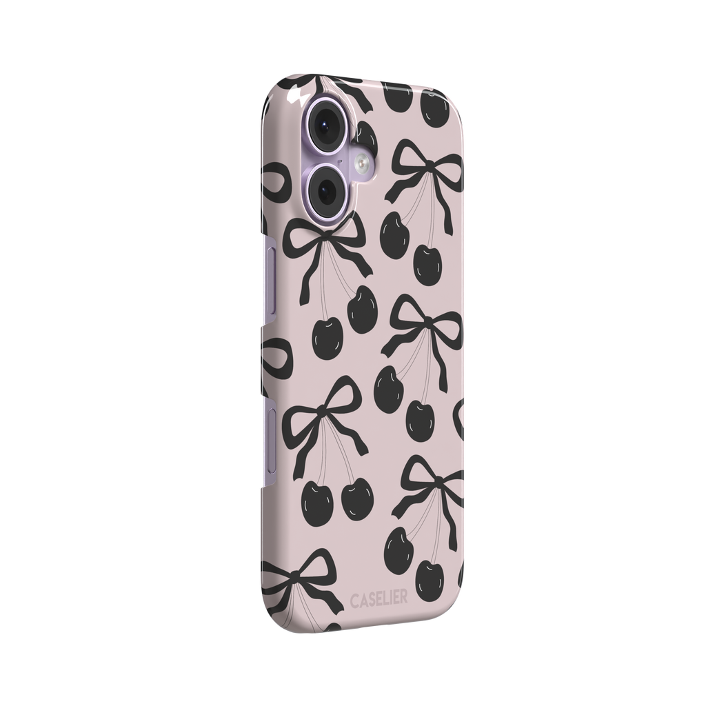 Black Cherry phone case with an all-over pattern of black cherries and ribbon bows on a blush pink background, phone case by Caselier — snap case, left view