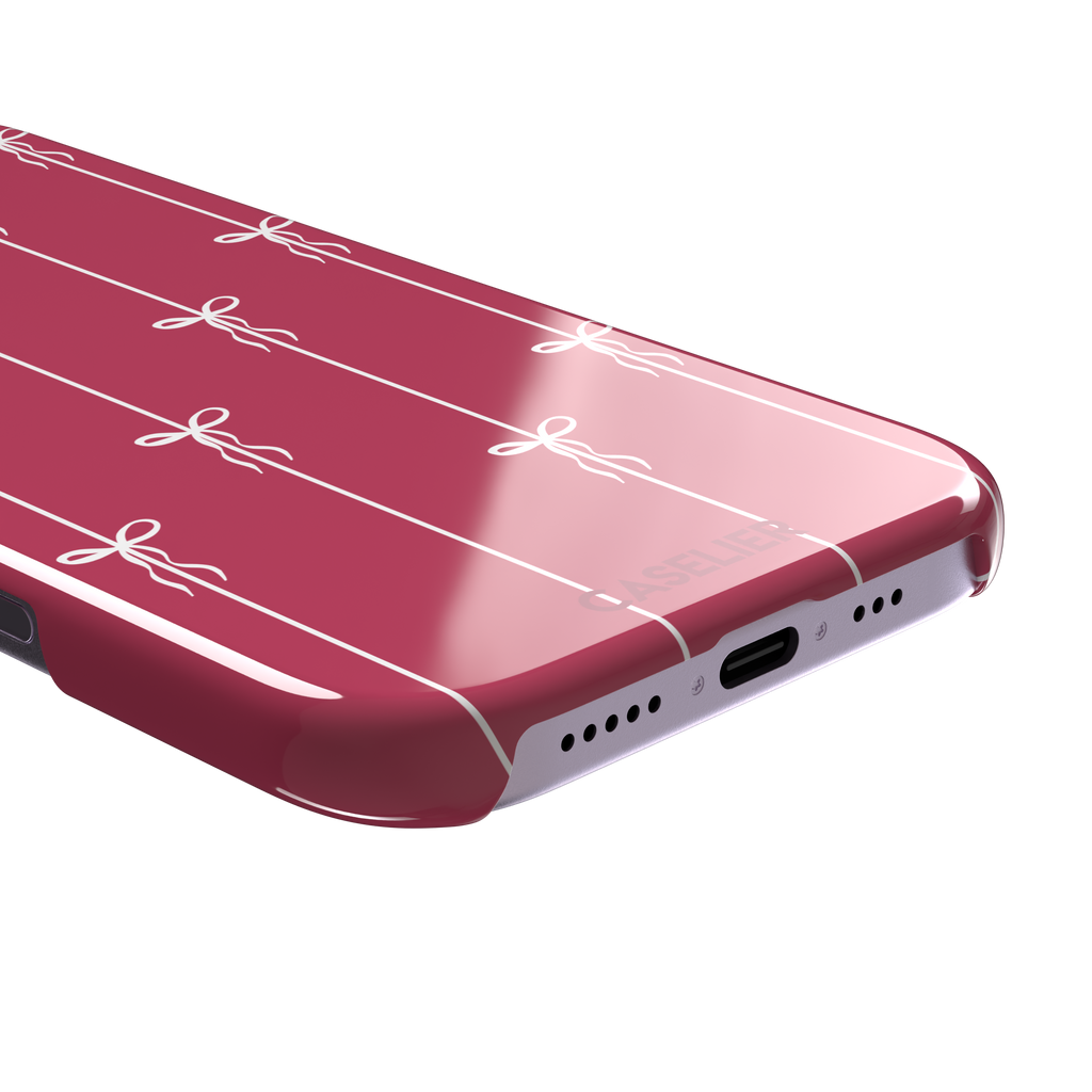 Bows on String phone case in raspberry pink with white ribbon bows tied along vertical stripes, phone case by Caselier — snap case, charging port detail
