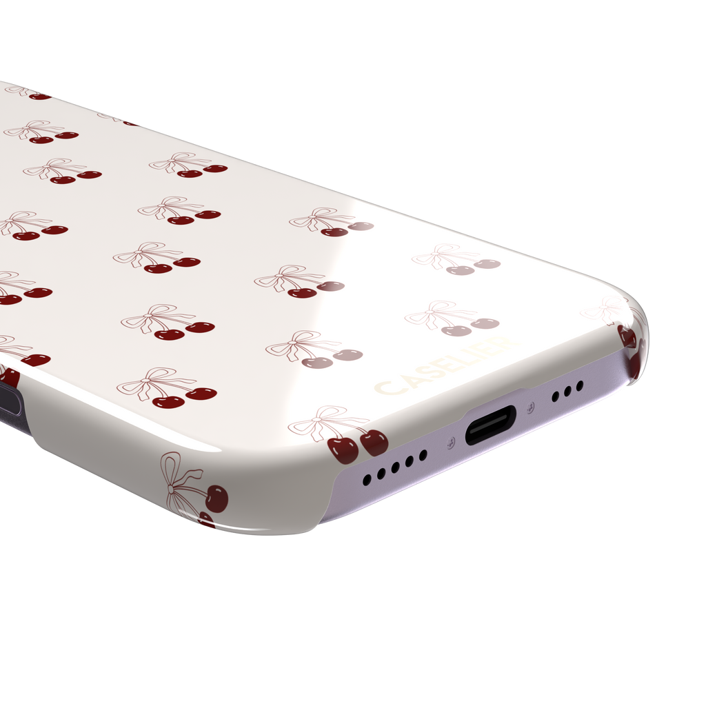 Cherry Bow phone case with glossy red cherries and delicate line-drawn bows scattered across a cream background, coquette style, phone case by Caselier — snap case, charging port detail