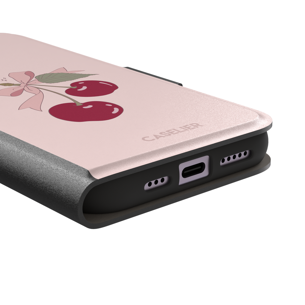 Soft pink phone case featuring two glossy red cherries tied with a pink ribbon bow and green leaf illustration in a coquette style, phone case by Caselier — wallet case, charging port detail