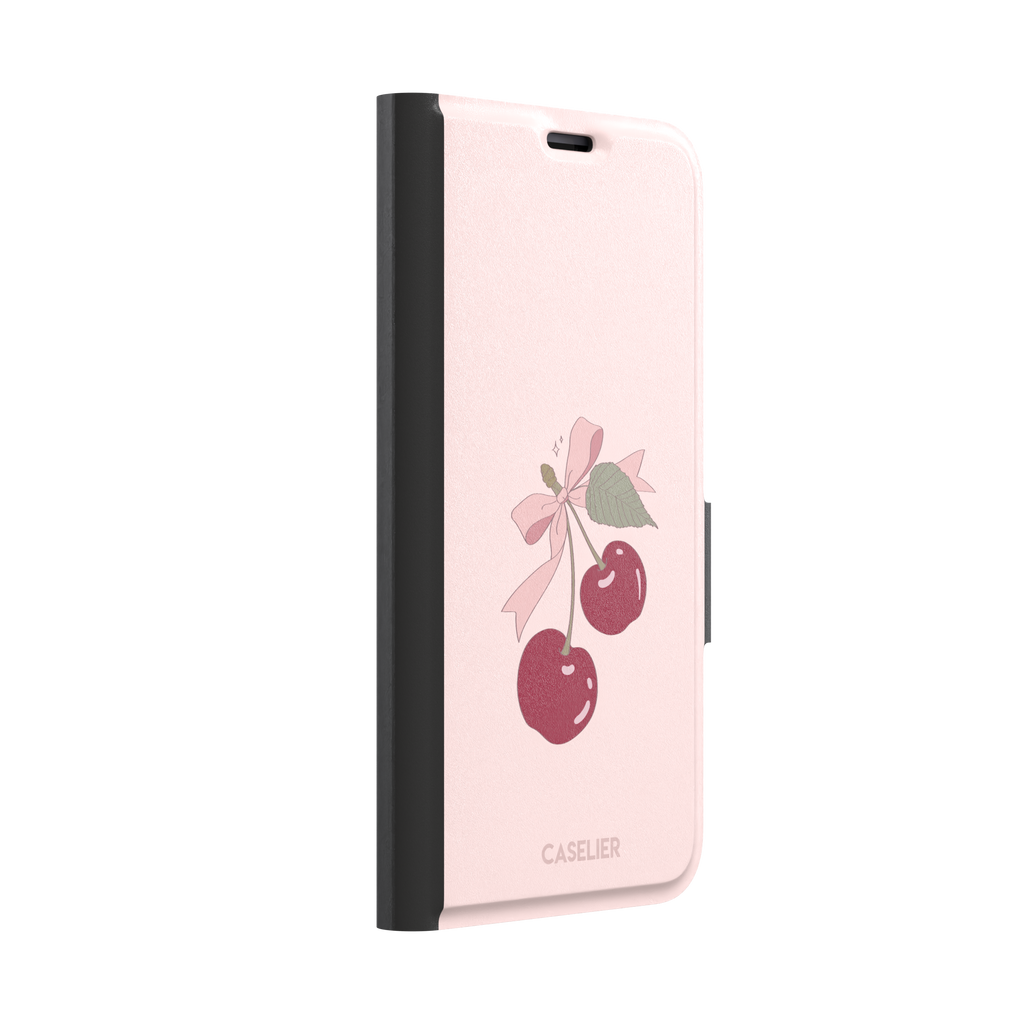 Soft pink phone case featuring two glossy red cherries tied with a pink ribbon bow and green leaf illustration in a coquette style, phone case by Caselier — wallet case, left view