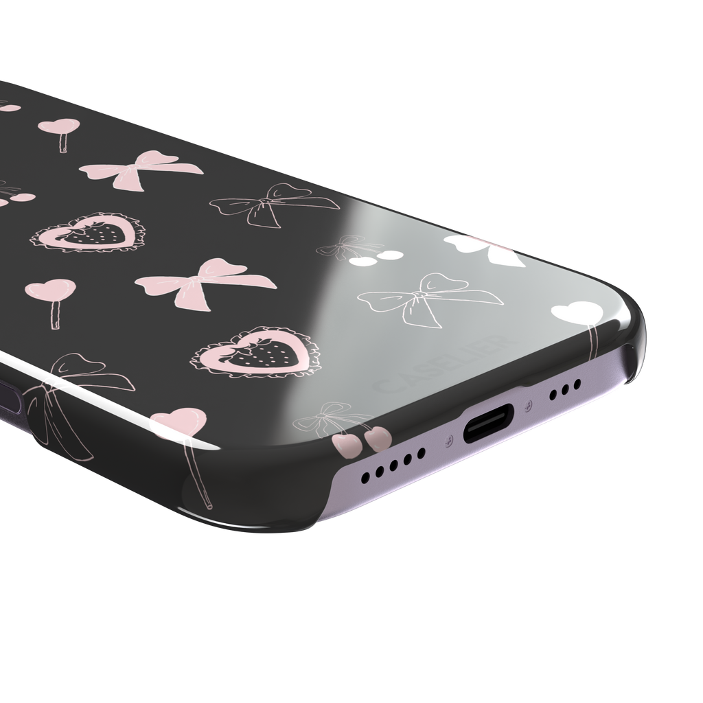 Sweetness Overload phone case in dark charcoal grey with pink bows, cherries, heart lollipops and frilled strawberry heart illustrations — snap case, charging port detail