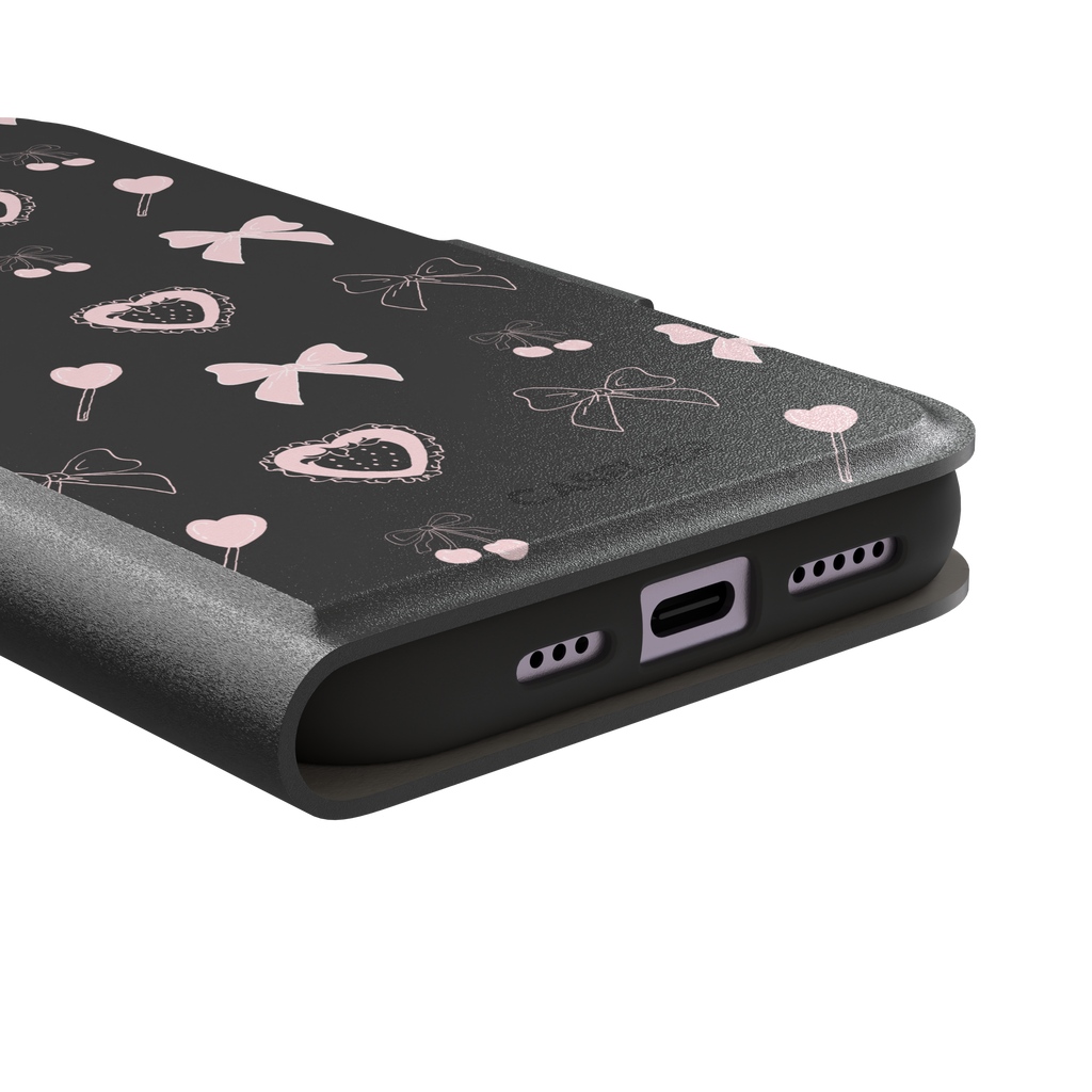 Sweetness Overload phone case in dark charcoal grey with pink bows, cherries, heart lollipops and frilled strawberry heart illustrations — wallet case, charging port detail