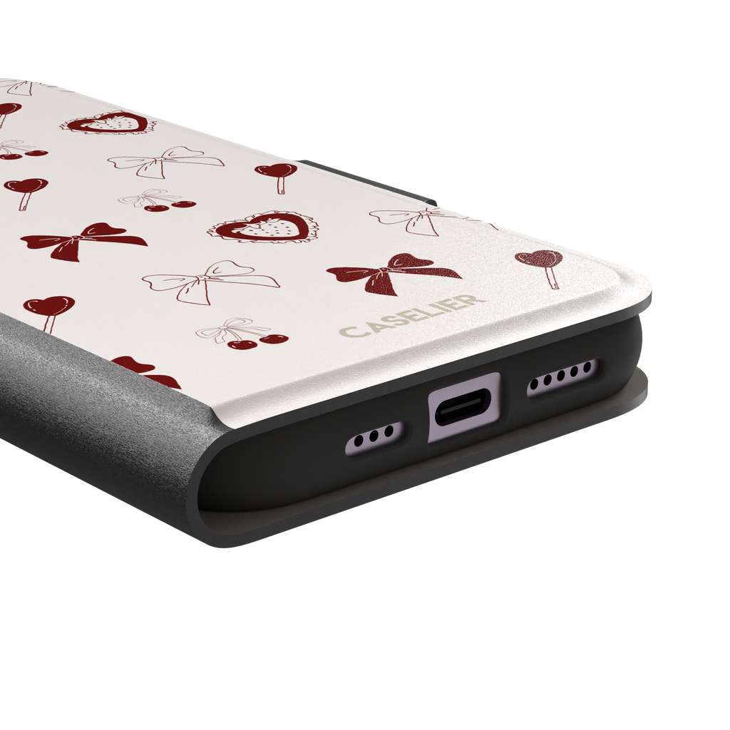 Sweetness Overload phone case in cream white with deep red bows, cherries, heart lollipops and frilled strawberry heart illustrations — wallet case, charging port detail