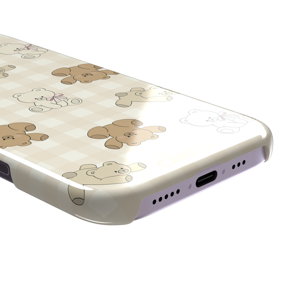 Teddybears phone case in warm cream with illustrated beige and ivory teddy bears scattered over a gingham grid pattern, some bears wearing soft pink bows — snap case, charging port detail