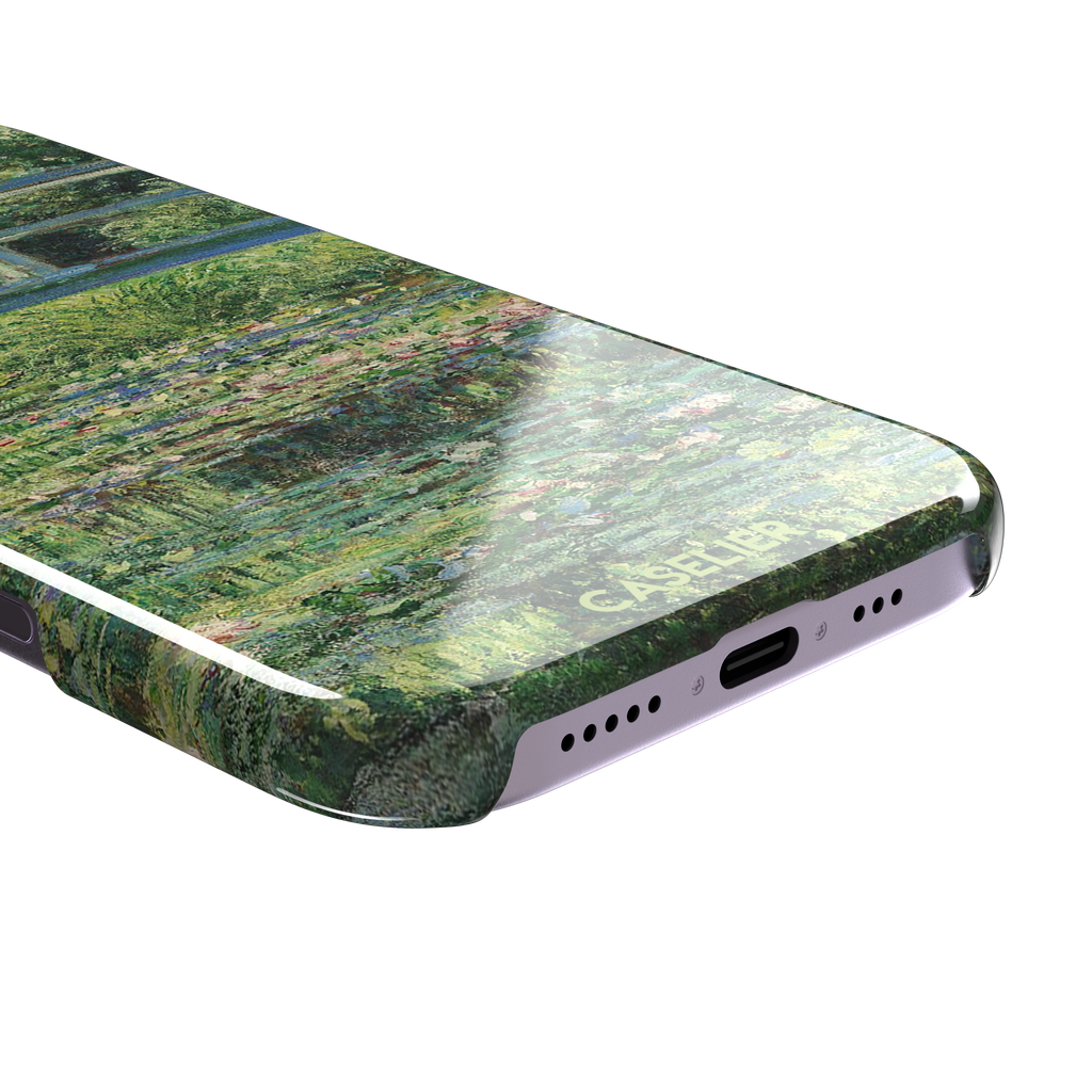 The Water Lily Pond by Claude Monet phone case showing the Japanese bridge over a green lily-covered pond with soft impressionist brushwork in deep greens and pink water lilies, phone case by Caselier — snap case, charging port detail
